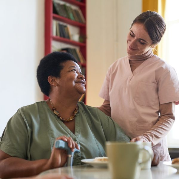 Portrait of smiling young woman assisting female patient during dinner at nursing home, copy space